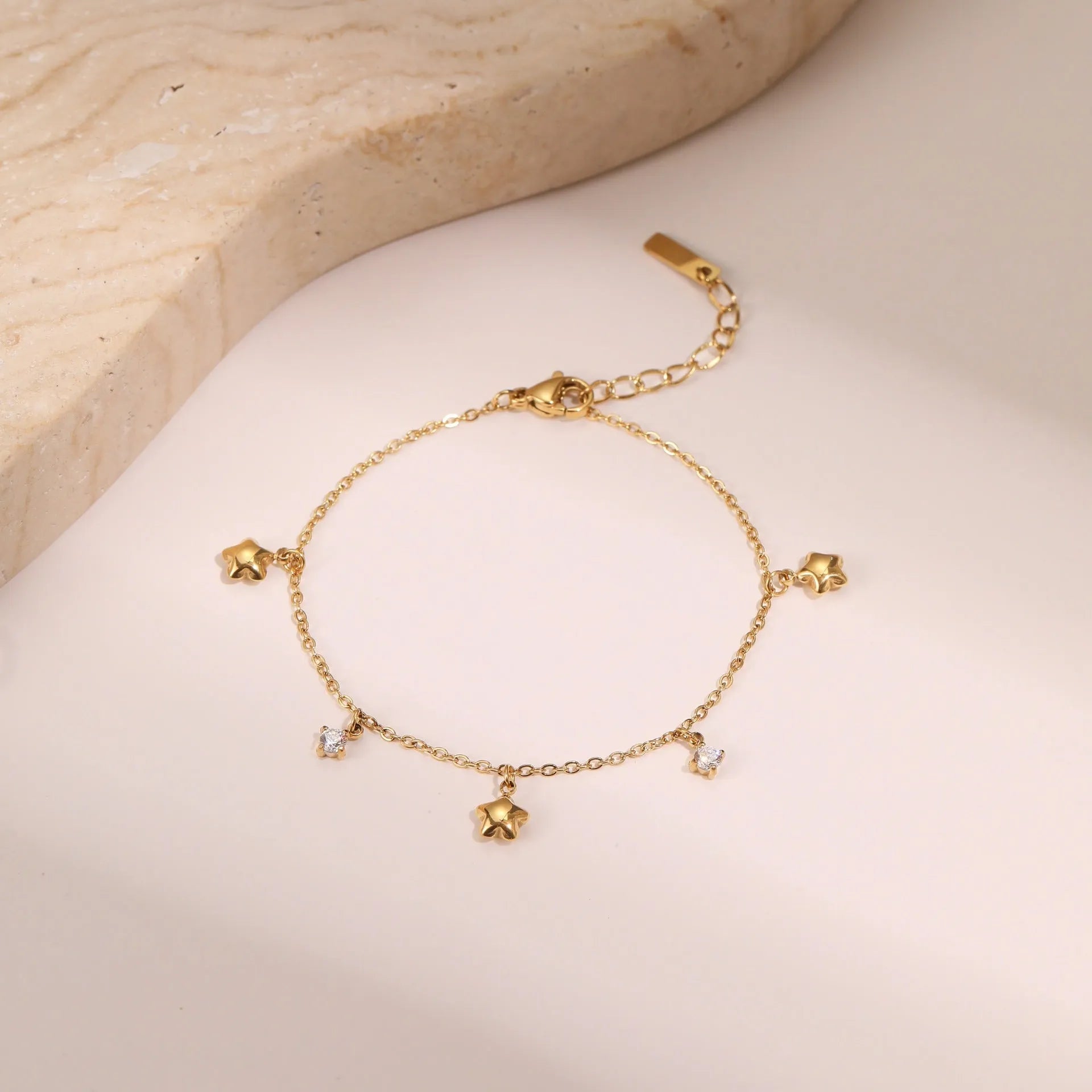 Gold plated stainless steel bracelet with a detailed zircon star pendant on a woman's wrist.
