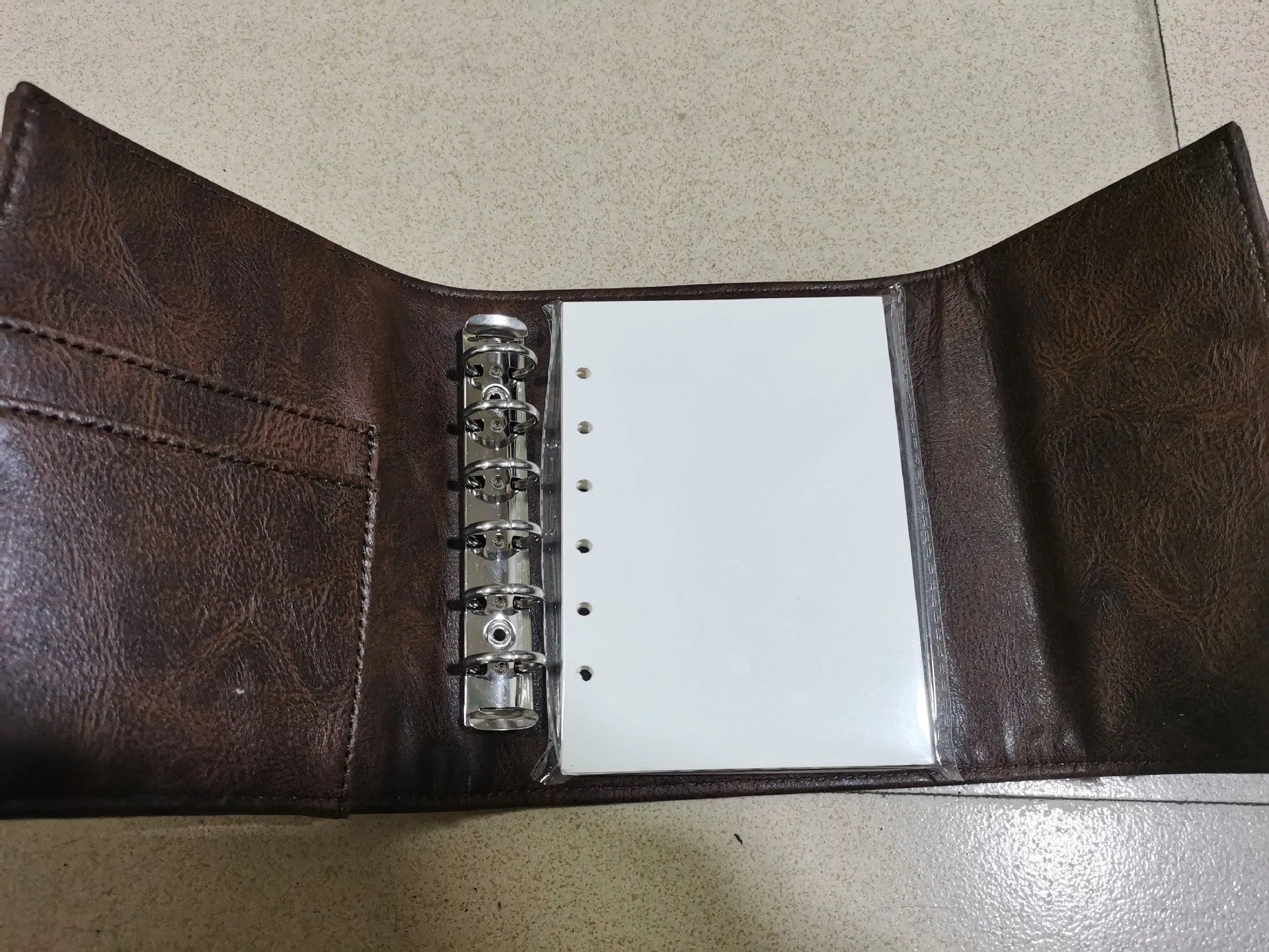 Brown PU cover A7 notebook with metal buckle closure showing loose-leaf binding and raw wood pulp pages