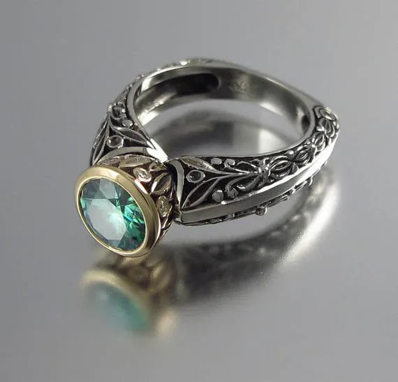 Gold-plated flower-shaped ring with a green gemstone on a silver-tone band, shown from above.