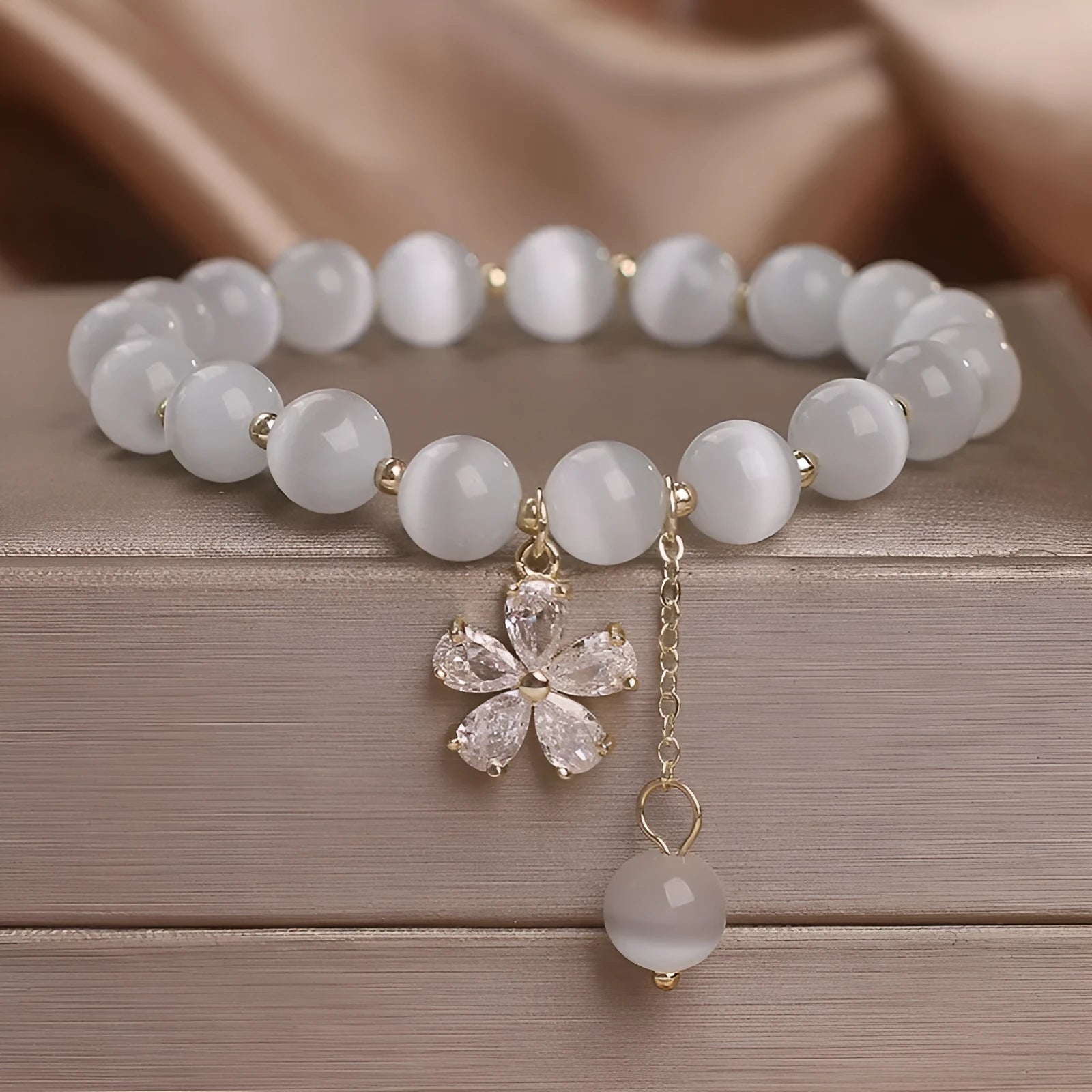 White cat's eye crystal bracelet with a silver flower tassel and safety buckle.