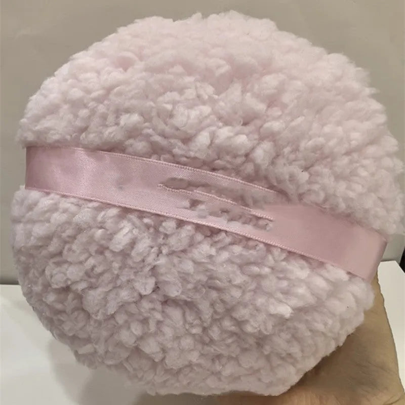 Large oval white plush powder puff for makeup on a plain background.