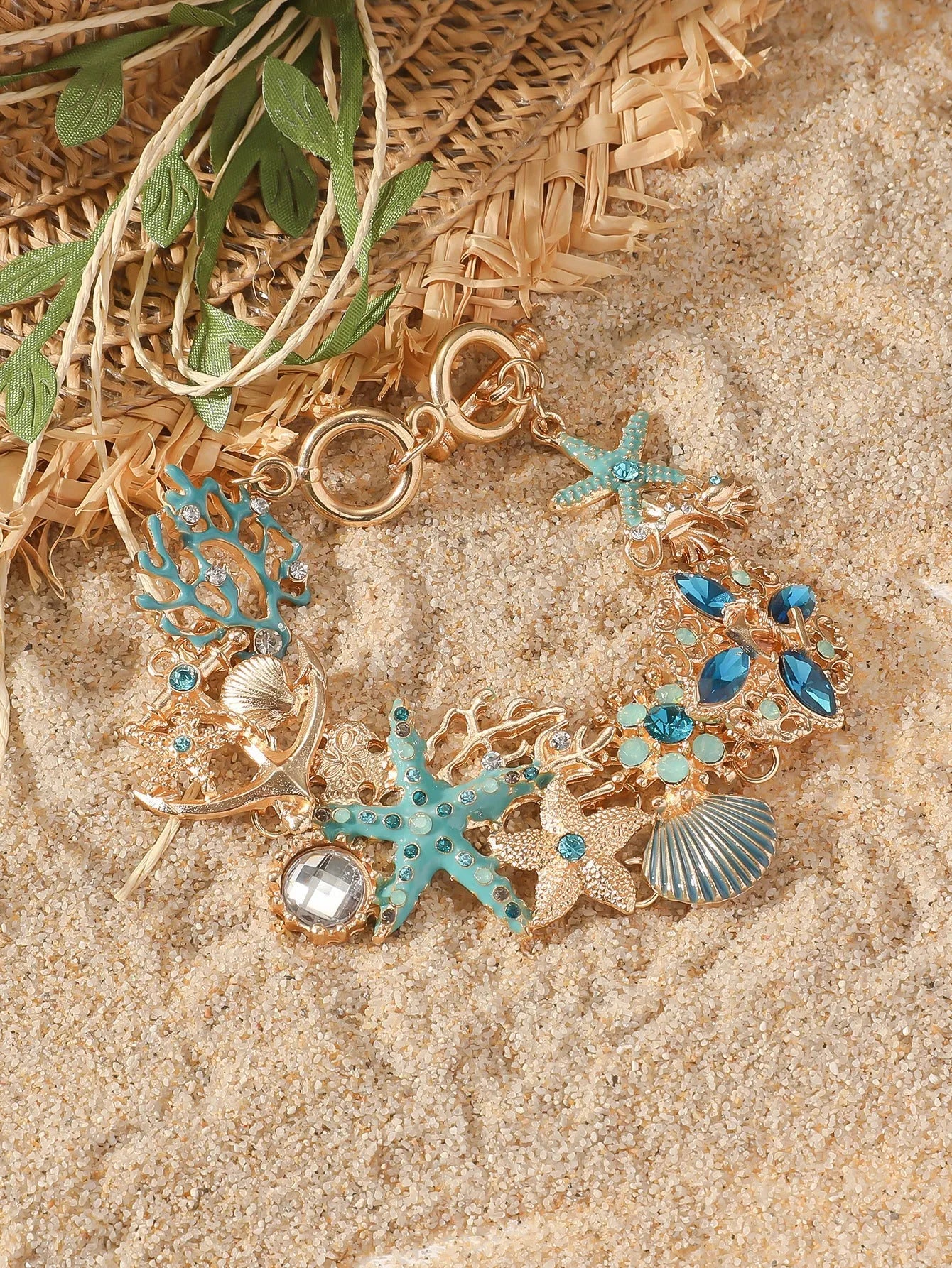 Close-up of a women's alloy bracelet featuring a boat anchor, marine shell, and starfish charms in a coral blue colour.