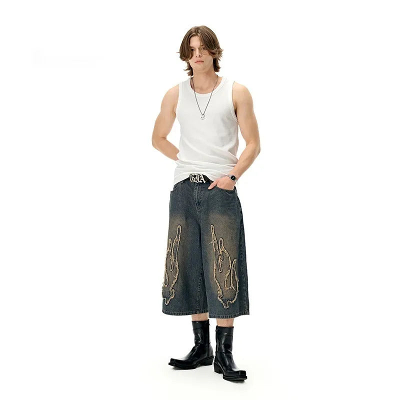 Men's black denim shorts with flame embroidery patches on the legs, showing a cropped, straight-leg cut.