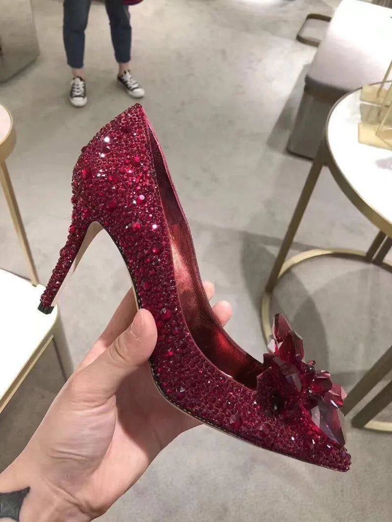 Gold women's high heels with pointed toe, rhinestone details, bow and stiletto heel on a plain background.