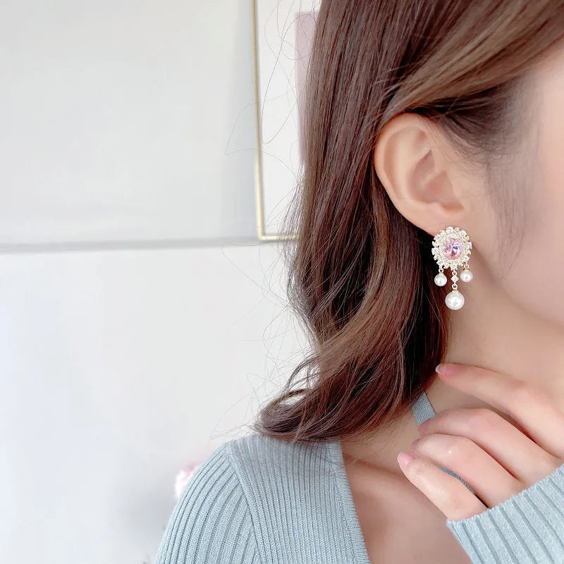 Oval-shaped geometric drop earring with a pearl tassel and inlaid zircon crystals in light purple.