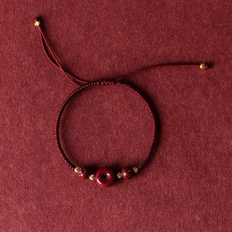 Heart-shaped cinnabar bead on an adjustable knot rope bracelet with a decorative peace buckle closure.