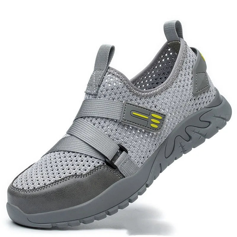 Men's grey safety work shoes with a woven upper and thick rubber sole on a work site background.